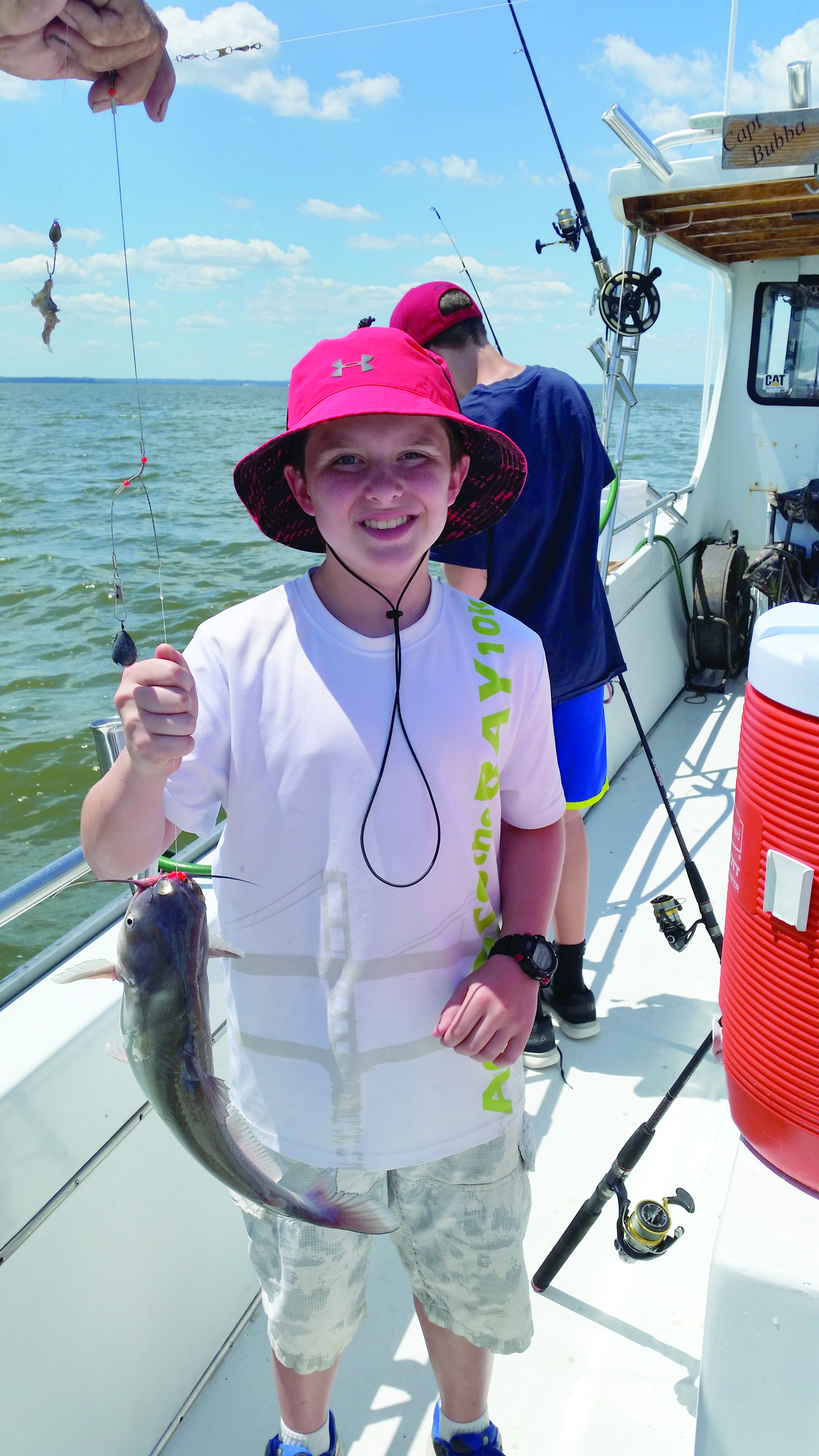 young camper holds up a fish caught while fishing at camp